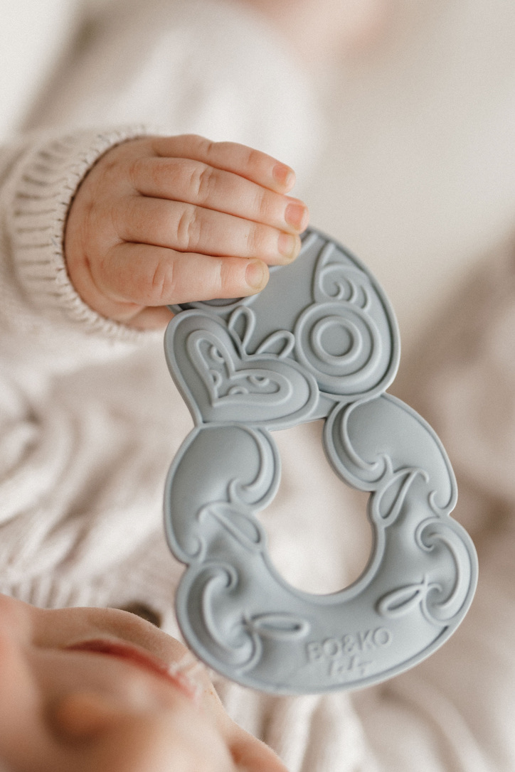 Baby Teether shaped in a tiki shape held by a baby