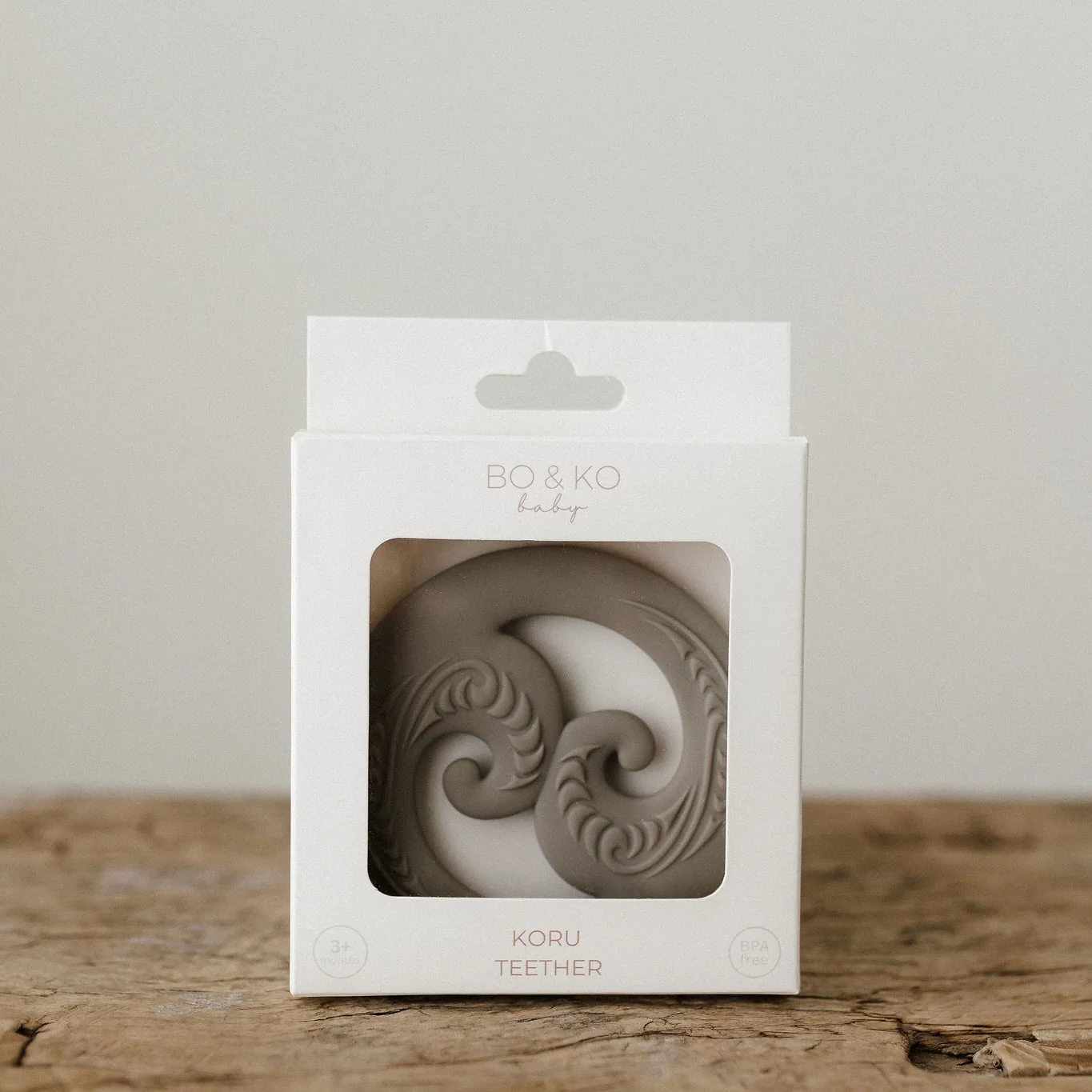 Maori inspired baby teether in white box  on a wooden stool 