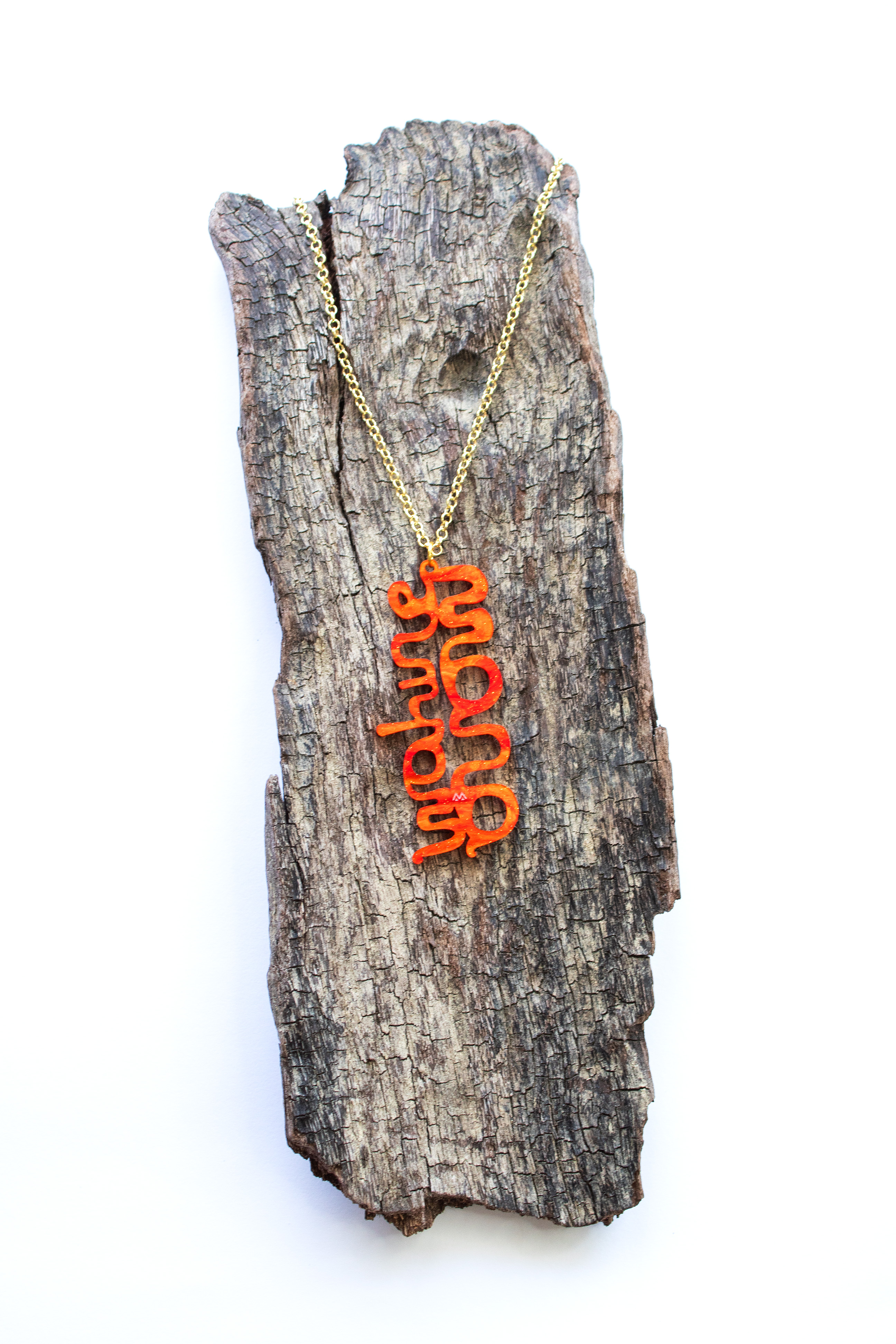 Orange Mana Wahine necklace on a piece of driftwood