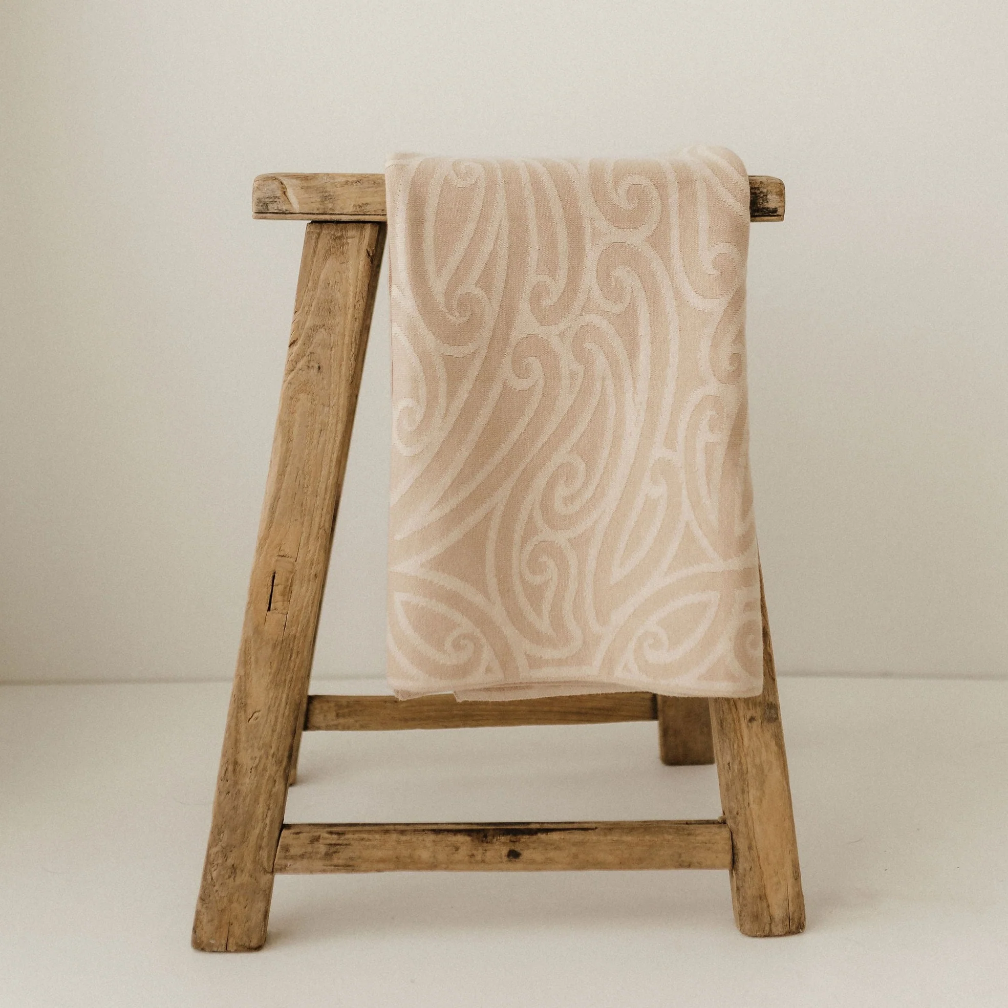Maori inspired babyb blanket draped over a rustic wooden stool