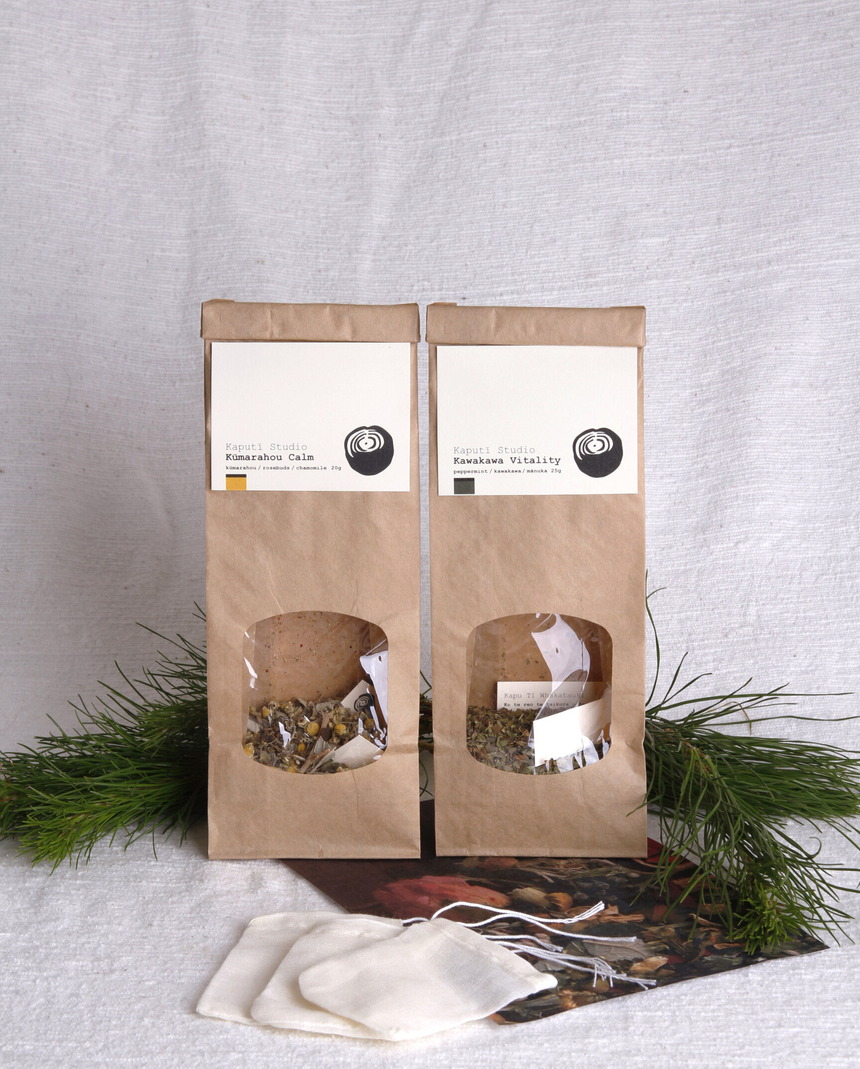 Two brown bags of loose leaf tea next to greenery and a white linen background